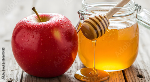 A shiny red apple covered in water droplets sits on a rustic wooden table next to a glass jar of golden honey and a wooden dipper. Generative AI