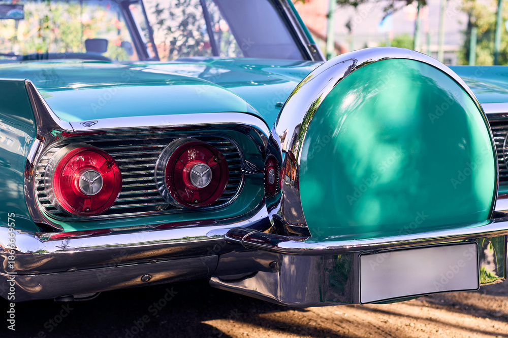 Fototapeta premium Red taillights of a beautiful turquoise vintage car. Well-maintained and well-painted vehicle, refurbished. Viewed from behind. Parked in an outdoor park at sunset, with natural light.