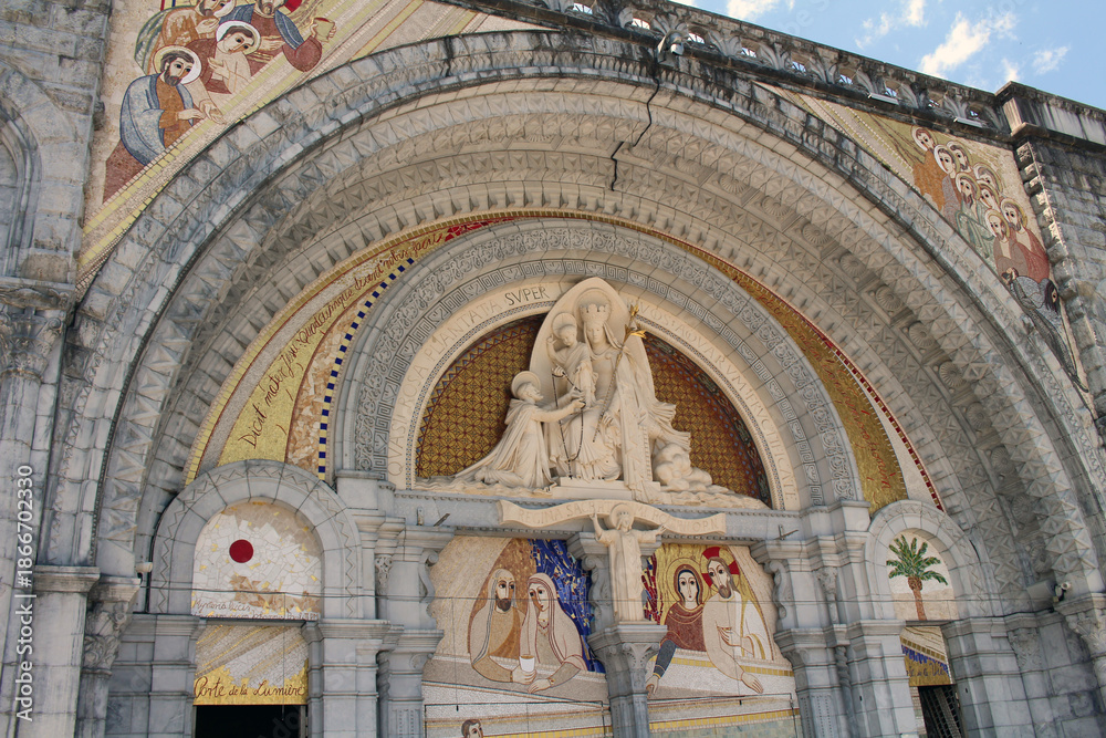 Obraz premium Entrance of the Basilica of Our Lady of Lourdes with mosaic artwork depicting Jesus, Mary, and saints, taken in July 2024.