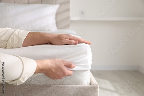 Foto Man putting bed sheet on mattress indoors, closeup