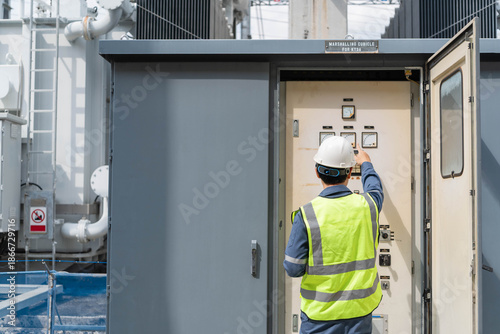 Foto Electrical engineer in safety vest pointing and inspecting control panel gauges inside Marshalling Cubicle at power substation, monitoring industrial energy system for grid maintenance