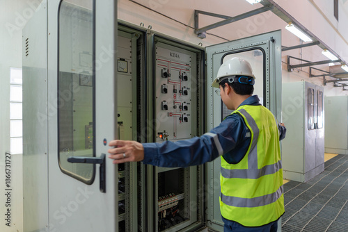Electrical technician opens control cabinet in a power facility, performing switching checks and system verification to ensure safe operation reliability and maintenance readiness.