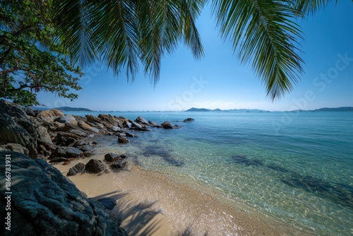 Tropical beach scene with palm fronds, rocks, clear water, and distant islands