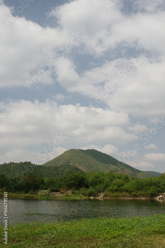 Beautiful outdoor view at Huai Tha Khoei Ban Kha Ratchaburi reservoir. The scene features a wooden photo spot, white ducks, and a calm lake with mountain views.