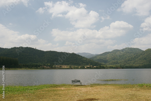 Beautiful outdoor view at Huai Tha Khoei Ban Kha Ratchaburi reservoir. The scene features a wooden photo spot, white ducks, and a calm lake with mountain views.