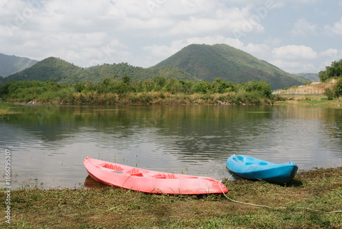 Beautiful outdoor view at Huai Tha Khoei Ban Kha Ratchaburi reservoir. The scene features a wooden photo spot, white ducks, and a calm lake with mountain views.