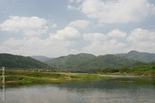 Beautiful outdoor view at Huai Tha Khoei Ban Kha Ratchaburi reservoir. The scene features a wooden photo spot, white ducks, and a calm lake with mountain views.