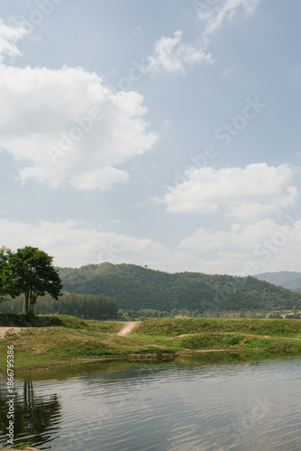Beautiful outdoor view at Huai Tha Khoei Ban Kha Ratchaburi reservoir. The scene features a wooden photo spot, white ducks, and a calm lake with mountain views.