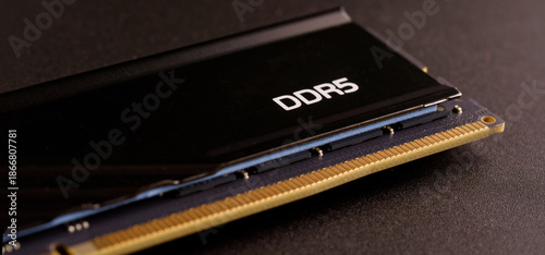 Macro shot of a DDR5 RAM stick showing the heat sink and circuit board on a dark surface. Concept of expensive electronic shortages and modern technology prices. Photo.