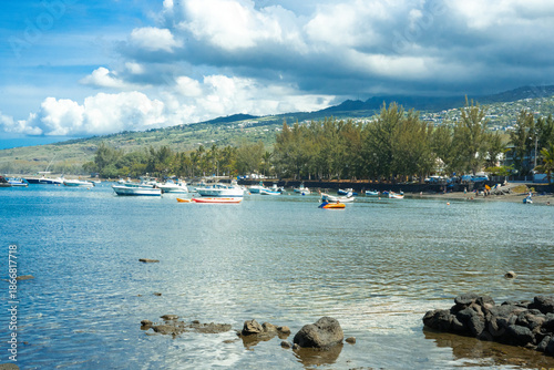Lagon et port de plaisance sur la côte de l’île de La Réunion.
Vue paisible sur un lagon tropical avec des bateaux au mouillage, une eau calme et peu profonde, des arbres côtiers et les reliefs verdoy