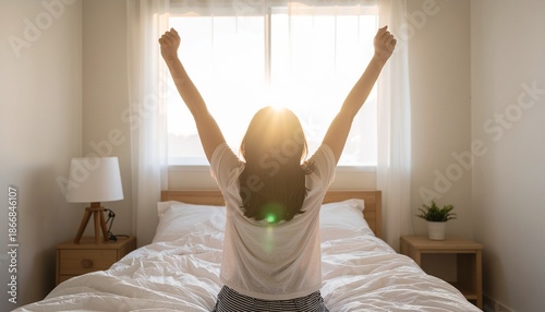 A person waking up in a bright bedroom, stretching with arms raised towards the sunny window, feeling refreshed and ready for the day.