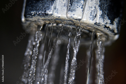 Close-up macro shot of water dripping from a faucet with mineral deposits
