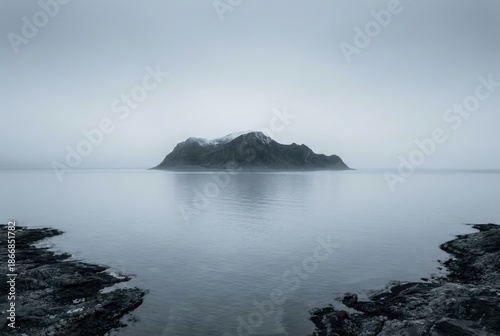 Rocky island in misty sea seascape, calm water and foggy horizon, framed by dark rocks, minimalist moody coastal landscape, solitude and tranquility concept
