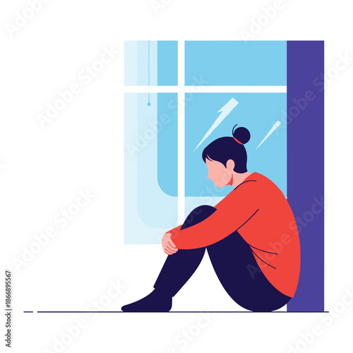 Lonely and sad woman sitting on the floor by a window and looking out into the distance during a gloomy or rainy day.