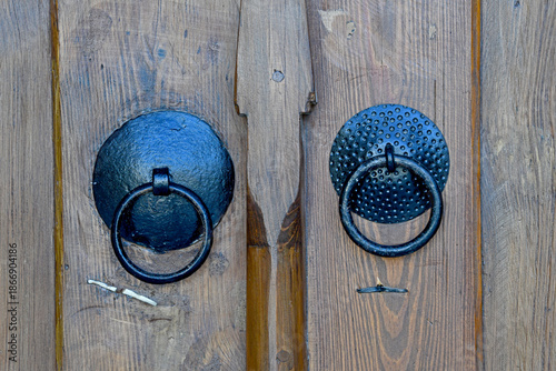 Obraz na plátně A close-up of two traditional black wrought iron ring knockers mounted on a weathered wooden door