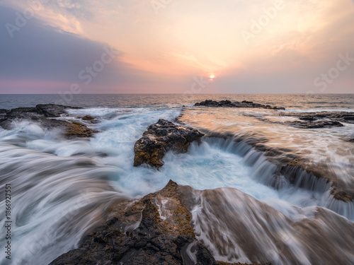 Long exposure seascape showing ocean waves cascading over volcanic lava rocks at sunset on the Kona Coast of Hawaii