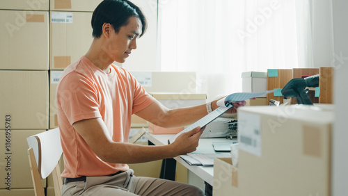 Foto Candid of young attractive Asia male entrepreneur E-commerce small business check sale purchase order from customer in document paper and inventory product ready shipping at small online retail shop