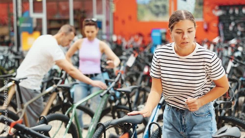 Smiling young girl choosing model seat on high-speed bike in modern sports shop