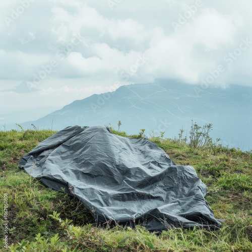 A dark sheet lies on grassy hill, overlooking distant mountain and cloudy sky