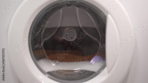 Foamy soap suds churning around shoes in washing machine drum, creating dynamic bubble patterns. Dense white foam envelops footwear during intense cleaning cycle.