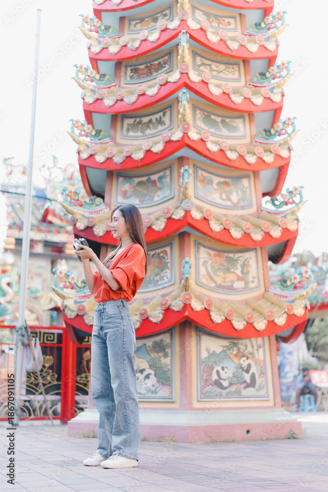 Obraz premium Woman tourist exploring Chinese temple, standing outdoors, capturing traditional architecture details of a colorful pagoda with her camera, enjoying a cultural travel experience