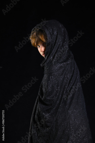 Person draped in shimmering black patterned fabric against dark background creating mysterious silhouette