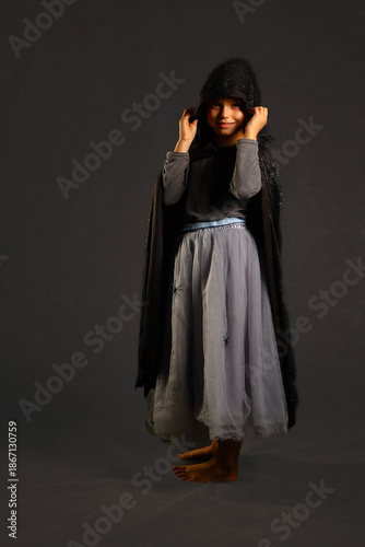 Small girl in spider‑themed costume holding hood, creating a sense of mystery and gentle eeriness