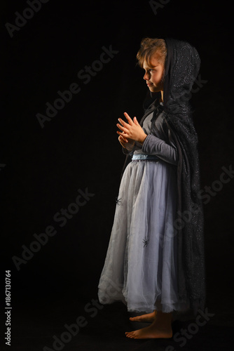 Mysterious little girl in a hooded spider costume standing in the dark, filled with quiet wonder and the promise of hidden fairy‑tale adventures