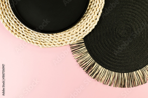 Top view of brown wicker table mat, black plate, black tray on pink background. Straw round tray, flat lay, copy space. 