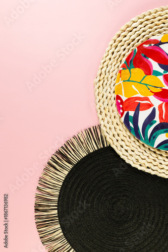 Top view of brown wicker table mat, black tray, colorful plate on pink background. Straw round tray, exotic plant plate, summer picnic. Flat lay, copy space. 