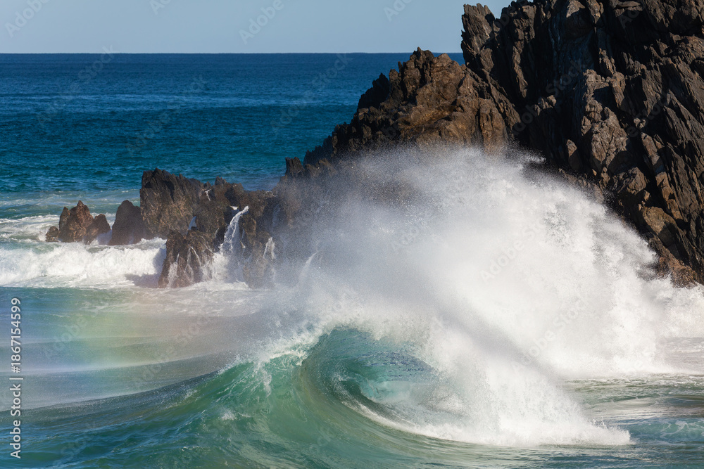 Obraz premium Waves crash against rocks at the mainland's easternmost point, creating rainbows in the ocean spray. Daylight, Byron Bay, New South Wales, Australia.