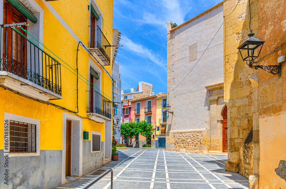 Fototapeta premium Villajoyosa old town narrow empty pedestrian street, Placa Esglesia square with typical colorful houses buildings in sunny summer day, La Vila Joiosa city historic centre, Valencian Community, Spain