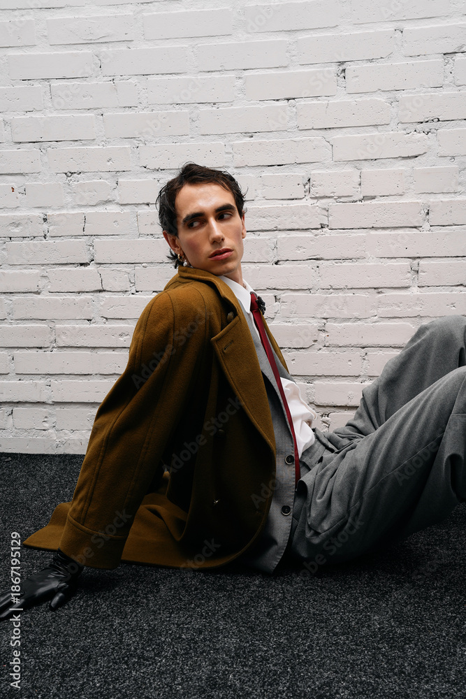 Naklejka premium Stylish man poses confidently in modern fashion setup with textured backdrop