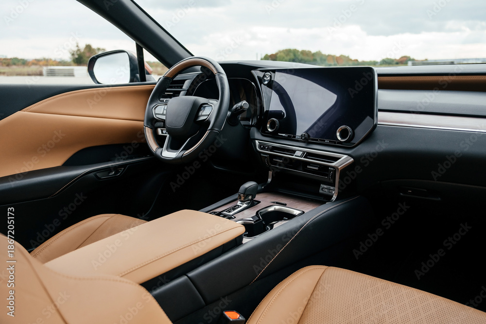 Fototapeta premium A premium, modern brown car interior, leather steering wheel, large navigation screen, air ducts, deflectors on the car panel. Interior details.
