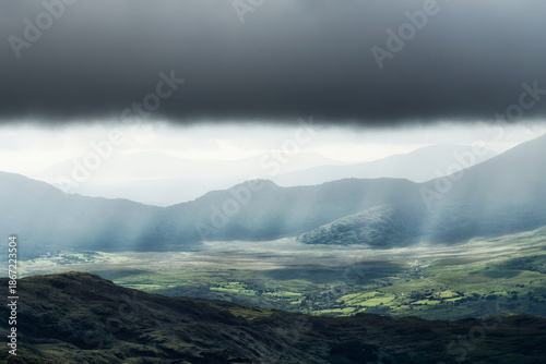 Overlook of a vast valley in County Kerry, Ireland with sun rays and clouds.