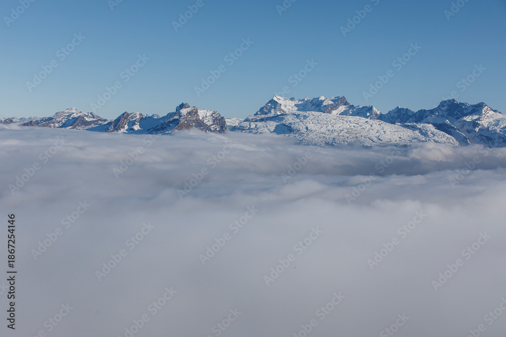 Obraz premium Majestic snow-covered mountains towering above a sea of clouds under a clear blue sky. A stunning la