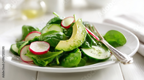 Fresh spinach salad with avocado, cucumber, and radish slices on a white plate. A vibrant and healthy salad featuring crisp spinach, creamy avocado, refreshing cucumber