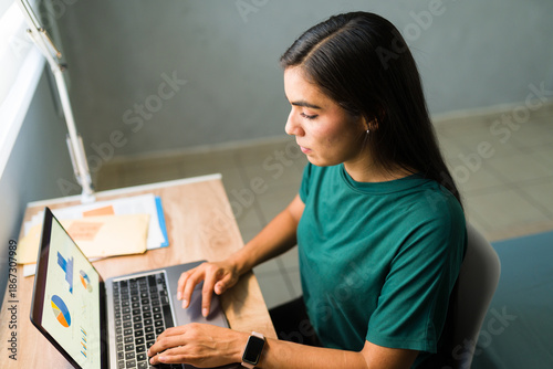 Foto Young woman analyzing business data and charts on a laptop in a home office, con