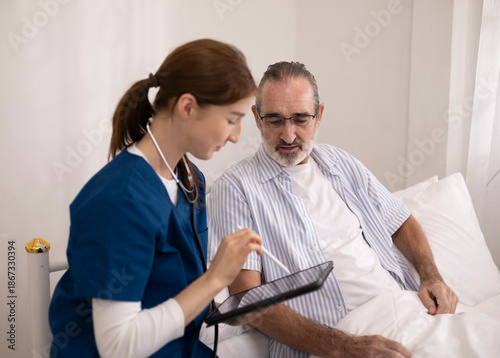 The elderly man is receiving care from a private nurse at home because of his illness. The nurse and patient are using a tablet for bedside consultations to manage their health.