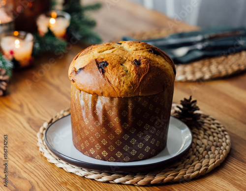 Traditional Italian panettone Christmas bread on festive decorated table with candles and holiday decor, dessert served on woven placemat