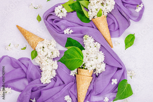 White lilac flowers in waffle ice cream cones on light stone concrete background. Flat lay