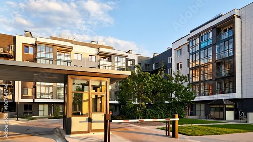 Modern apartment complex entrance with a gated security checkpoint surrounded by contemporary architecture and landscaped green spaces in the urban setting.