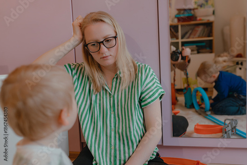 Fotografía Woman rests hand near head while child faces her, striped shirt with soft daylig