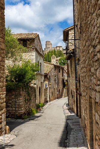 A winding alleyway in the medieval town of Assisi, Umbria, showcasing historic stone architecture under a bright sky. Assisi, Italy,