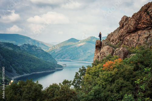 A woman on the top of a rock enjoys the view of an autumn forest and Studen Kladenec dam, Bulgaria