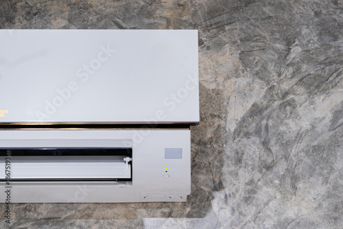 The white air conditioner is mounted on the concrete wall in the room.
