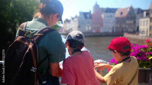 Family tourists using a map together, standing on a bridge by a canal with charming old buildings and colorful flowers, enjoying a lively summer city vacation