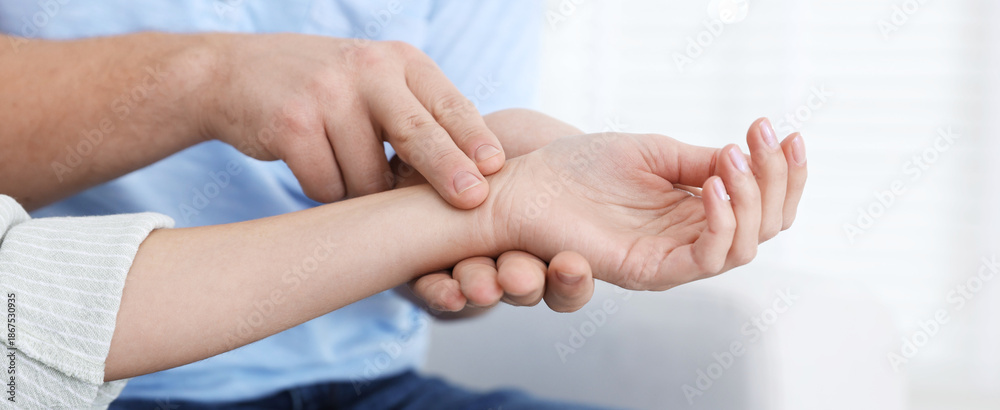 Fototapeta premium Man checking woman's pulse with fingers at home, closeup