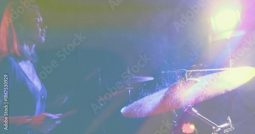 Striking drummer in dark v-neck hitting cymbal on spotlit stage, drumsticks and spray, copy space