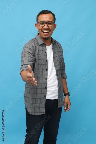 Middle age Asian man smiling looking at camera, handshake gesture, concept of getting acquainted, introducing yourself or congratulating, standing isolated on blue background.